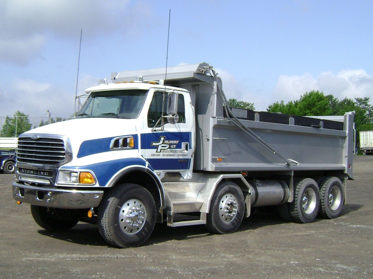 Camion à benne basculante blanc et bleu avec un lit argenté, stationné à l'extérieur.