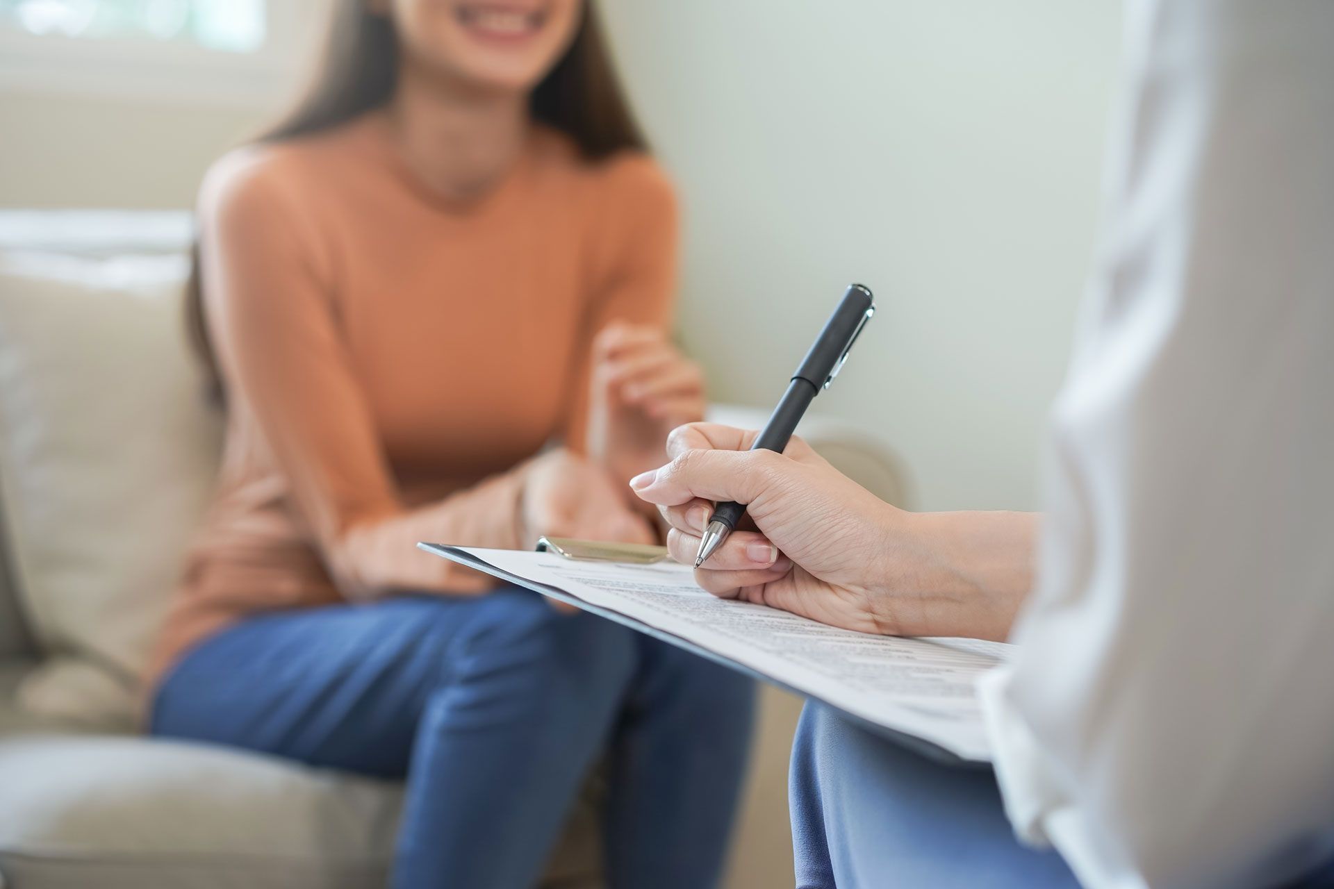 Therapist taking notes while a smiling patient sits on a couch.