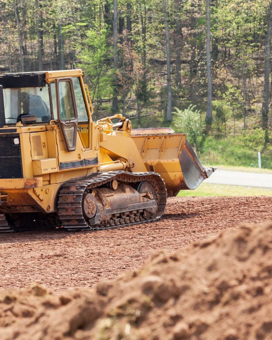 Yellow bulldozer grading soil, with trees in the background.