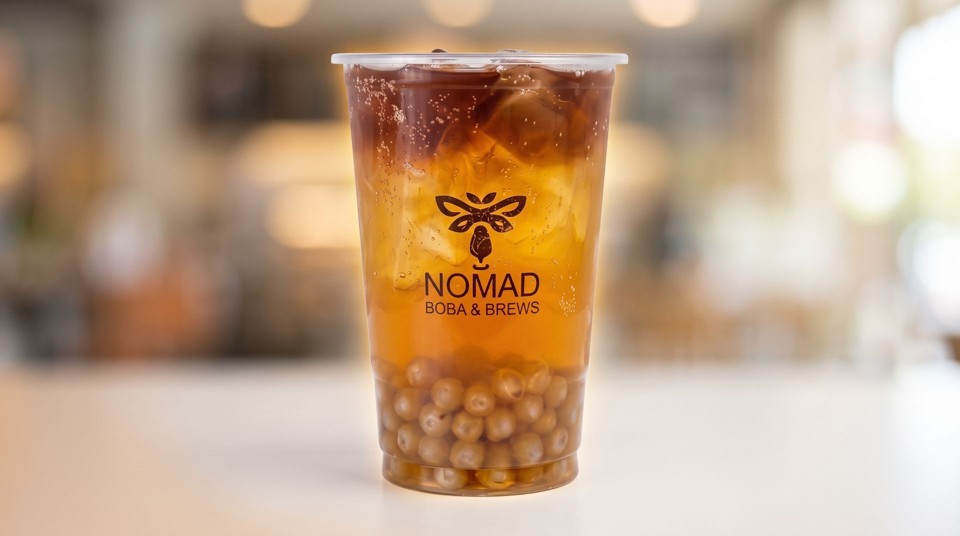 Clear iced coffee in a branded plastic cup with a domed lid and amber syrup inside, on a blurred café counter