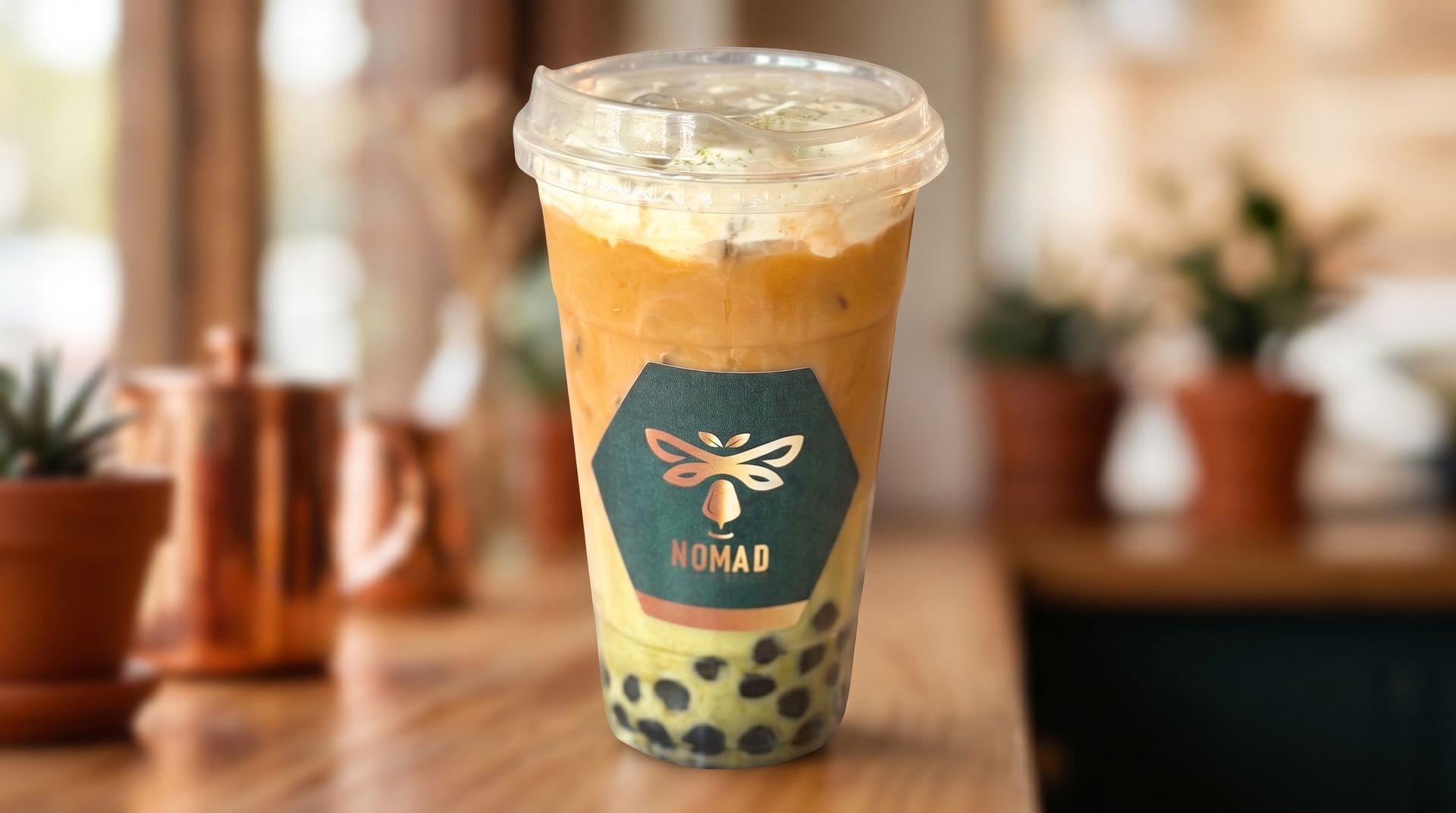 Boba tea in a clear cup with black pearls on a wooden table, softly blurred café background