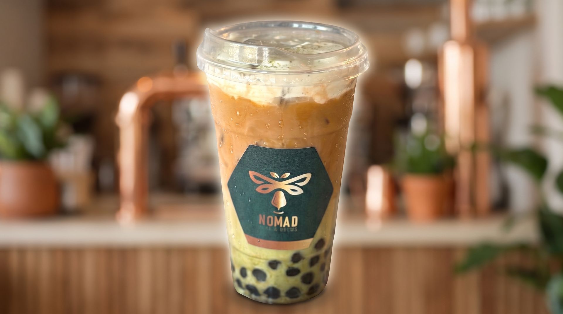 Bubble tea cup with black tapioca pearls and a teal label, on a blurred café counter.