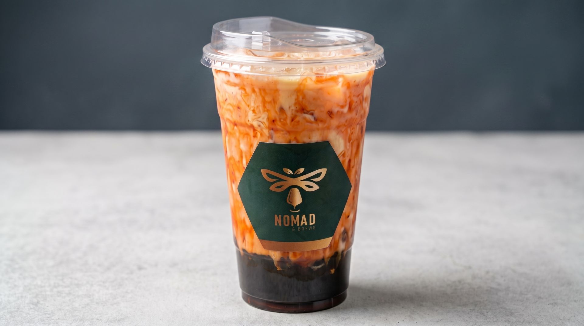 Iced orange-and-black layered drink in a clear plastic cup with a bee logo on a tabletop.