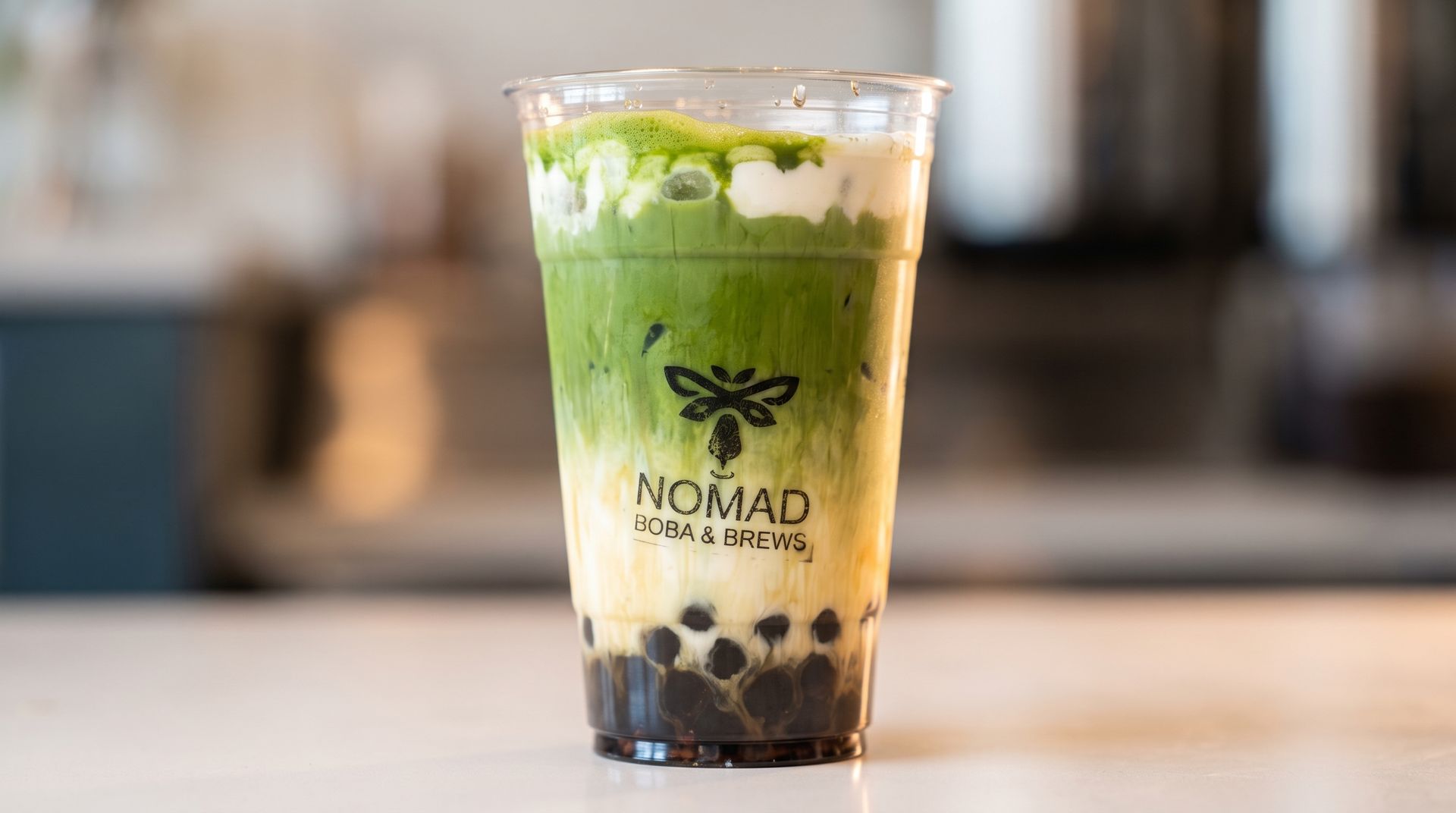 Clear plastic cup of matcha bubble tea with milk swirl and tapioca pearls on a counter