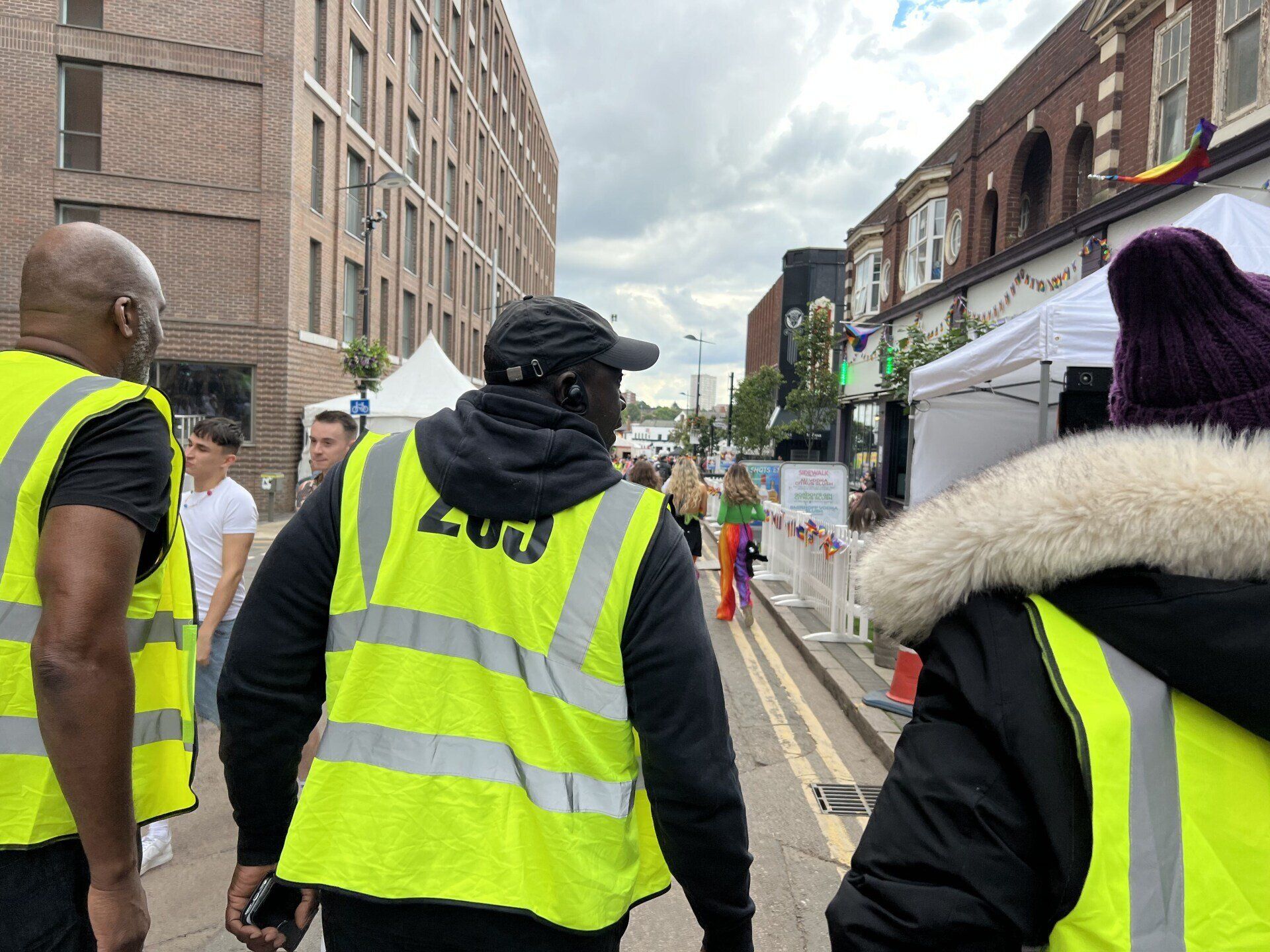 A group of people wearing yellow vests are walking down a street.