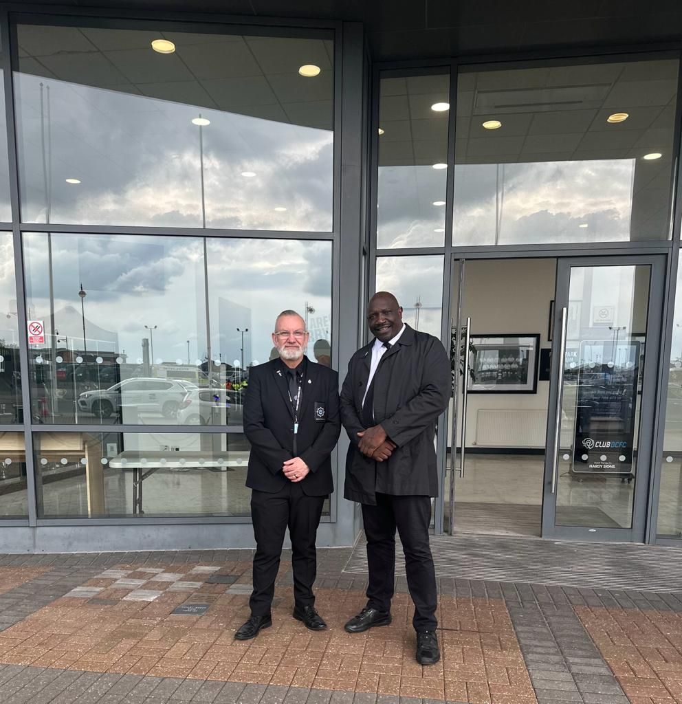 Two men in suits are standing in front of a building