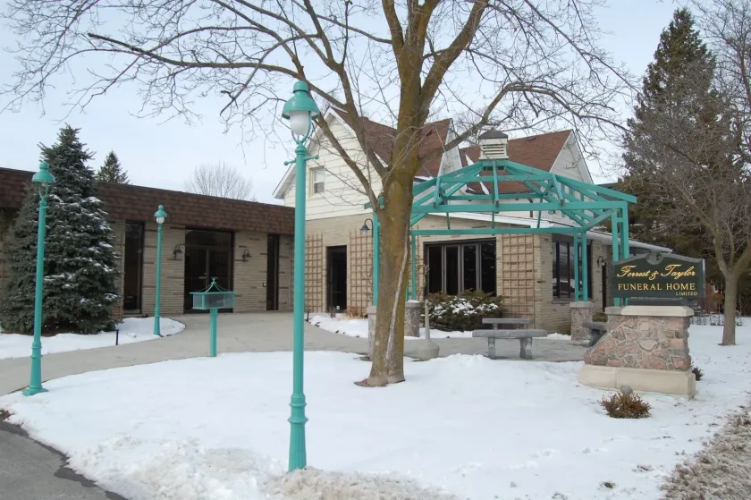 Snowy entrance to a stone building with a teal canopy and lamp posts.