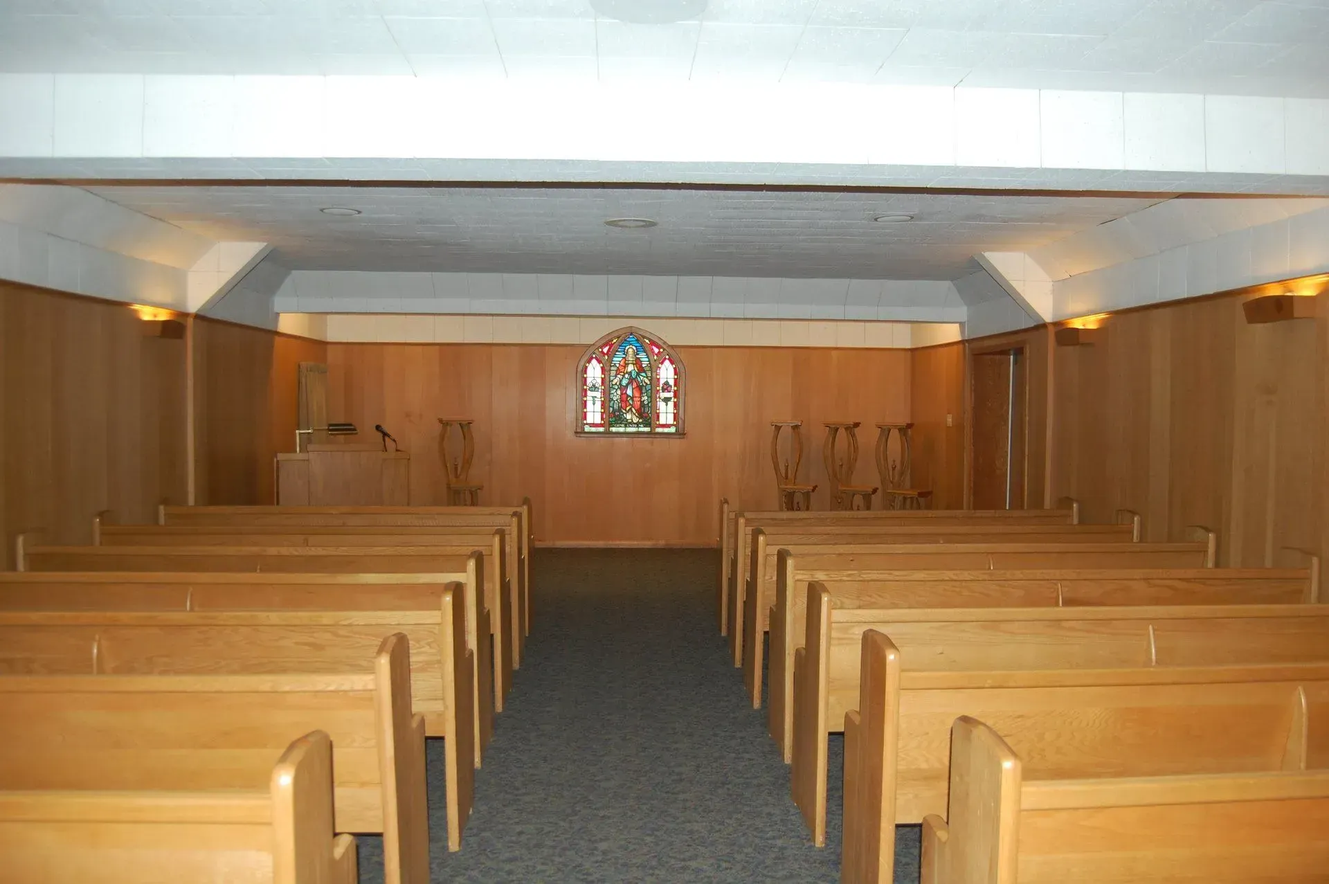 Empty wooden church chapel with pews facing a small stained-glass window at the front