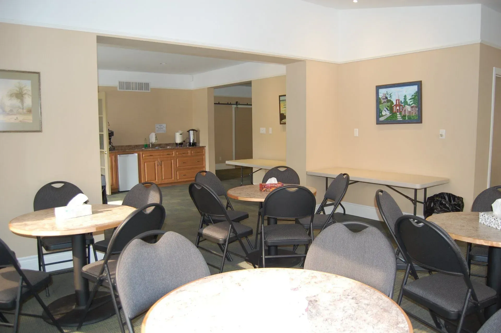 Empty dining room with round tables and black chairs, tan walls, and framed pictures.