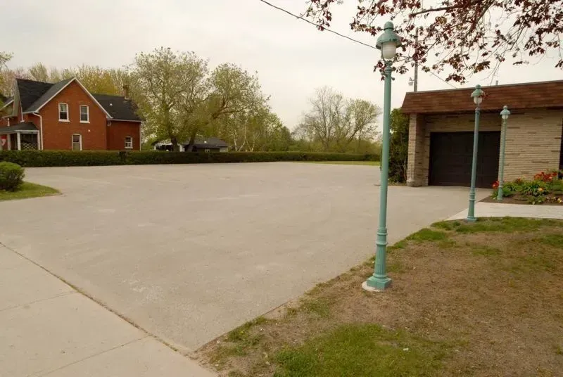 Wide empty paved lot beside a brick garage, with a green lamp post and red house in the background.