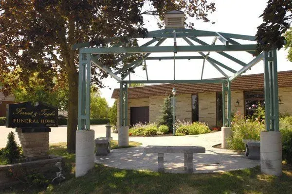 Covered entrance pavilion at a park or community center with a stone sign and bench seating