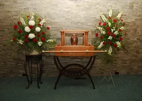 Wooden urn on a stand with two red-and-white floral arrangements against a brick wall