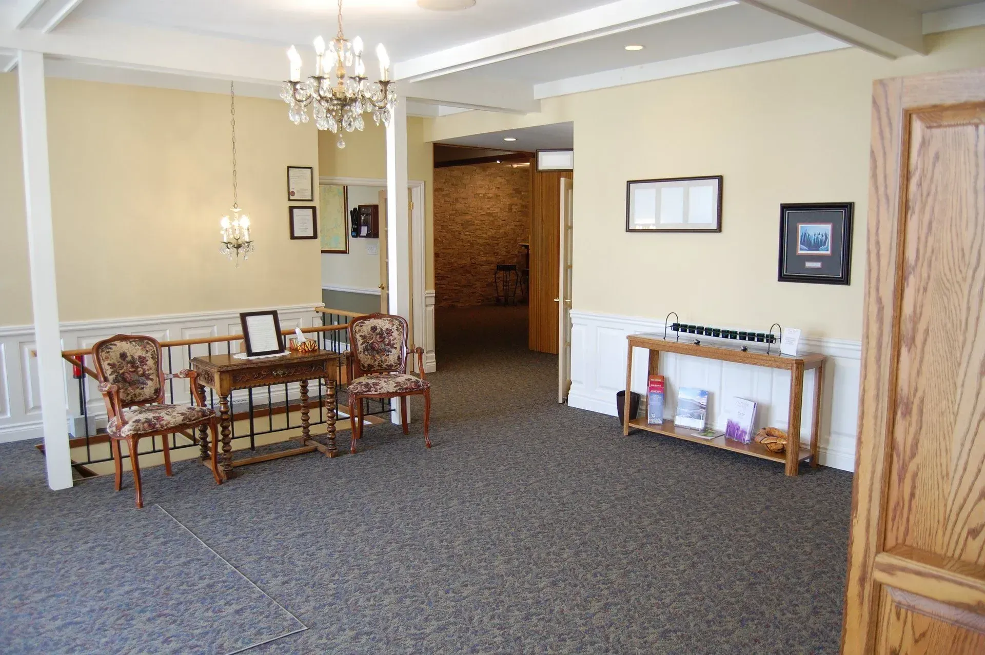 Waiting area with wooden chairs, chandelier, and framed wall art in a carpeted room