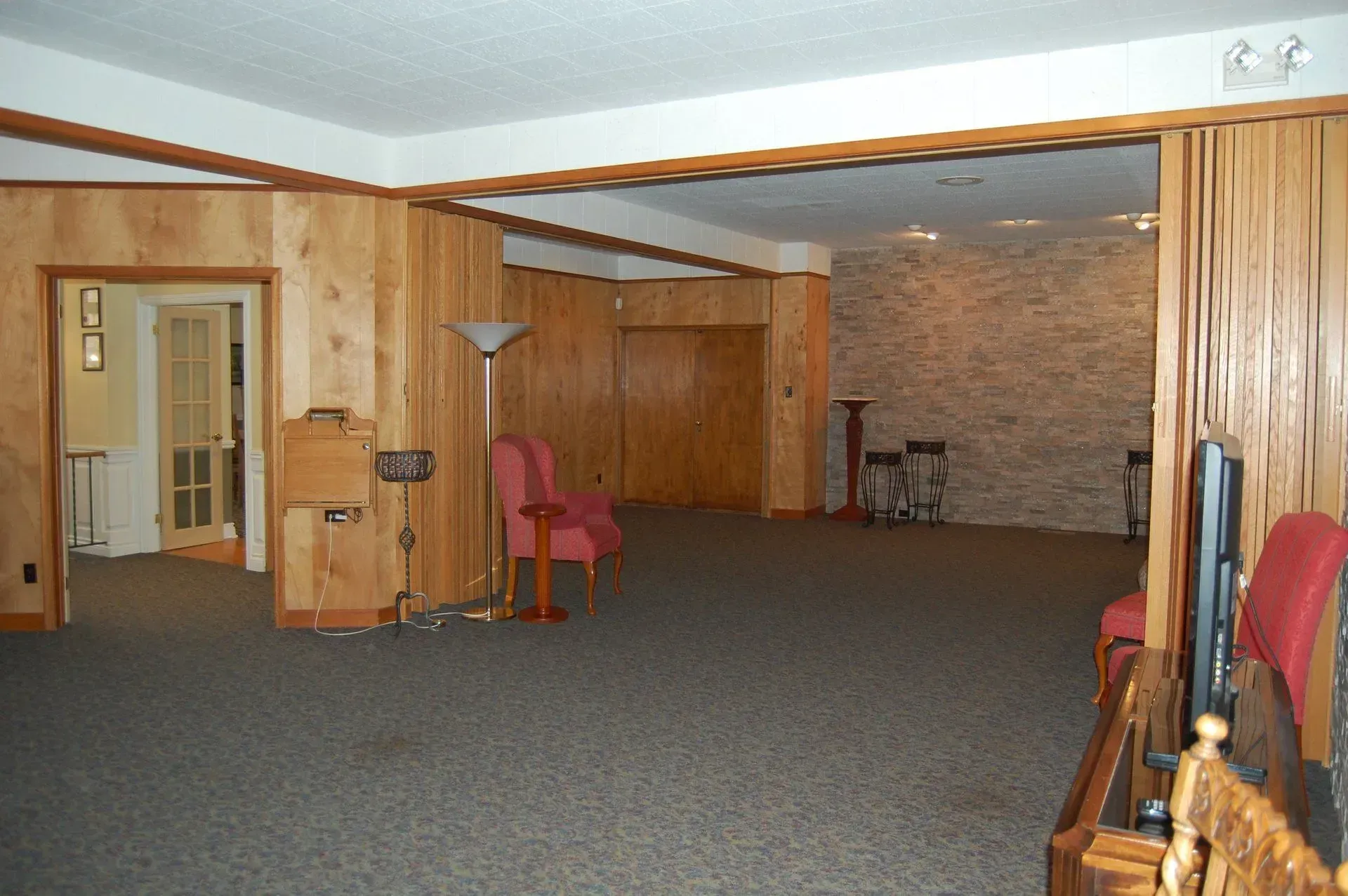 Empty basement rec room with carpet, wood-paneled walls, and a few chairs along the sides