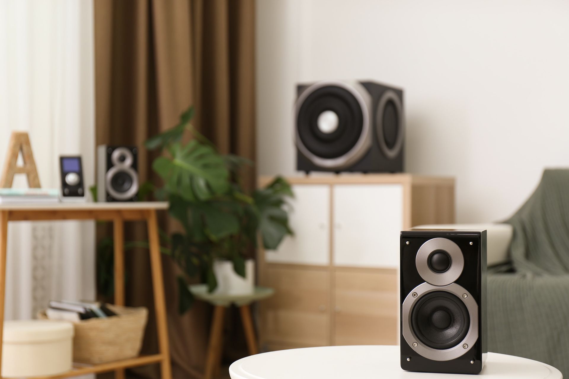 Speaker on a table in a room with speakers in the background. A green plant and a sofa complete the scene.