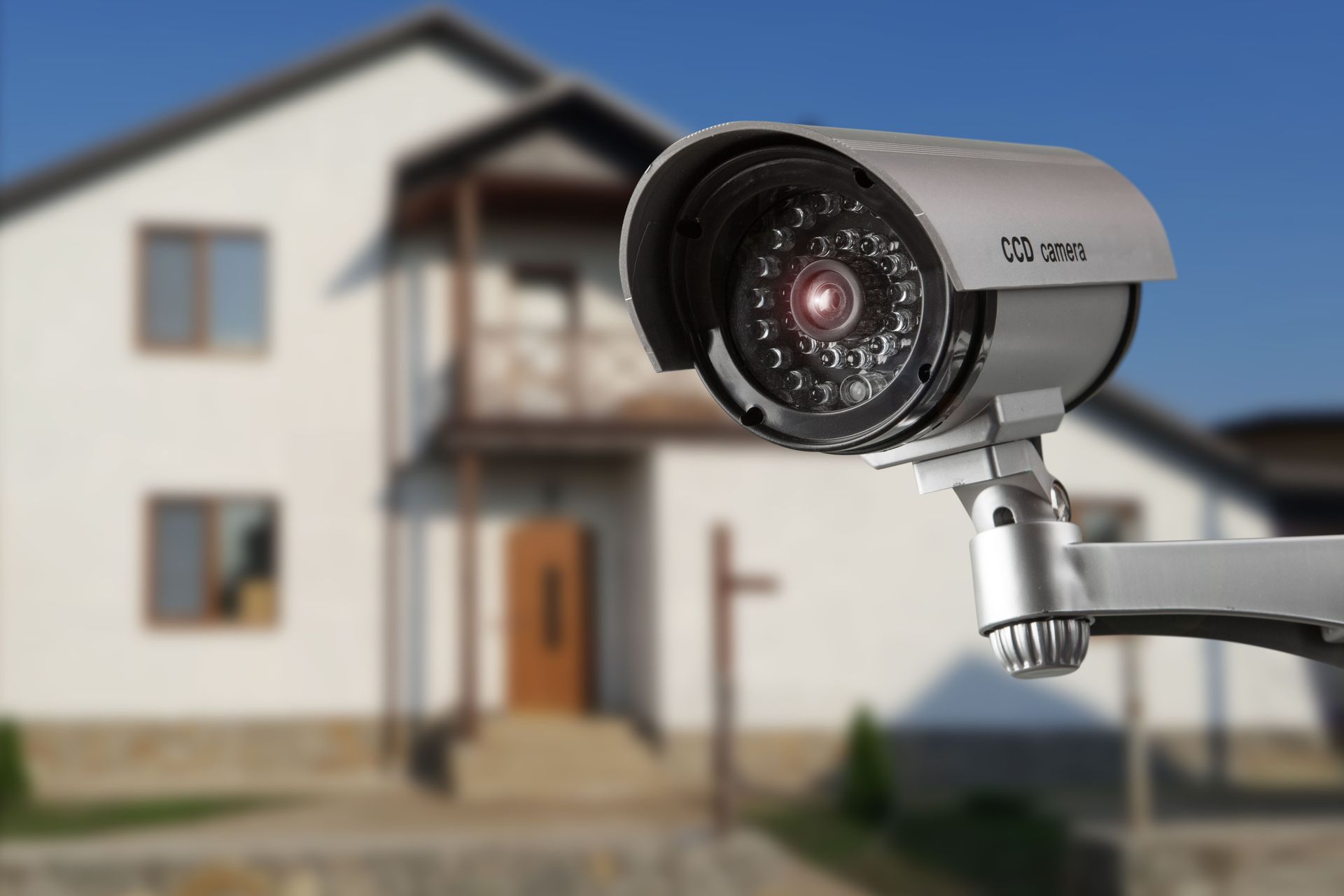 Security camera mounted outside a white house with a blue sky background.