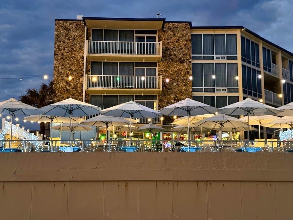 Hotel with outdoor seating, umbrellas, and string lights, at dusk.