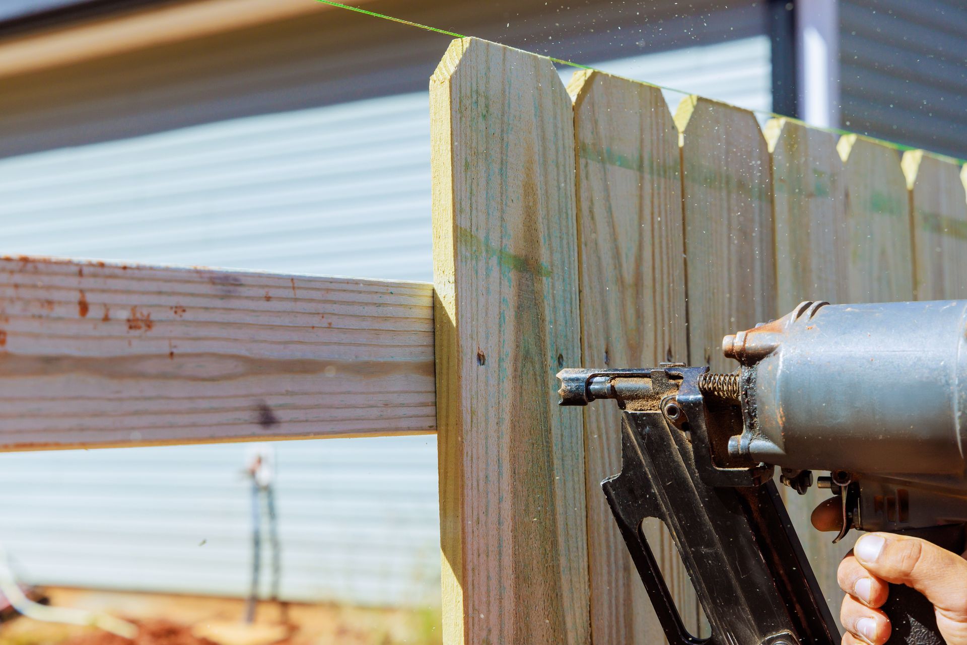Contractor installing a wood privacy fence rail with a nail gun during fence installation