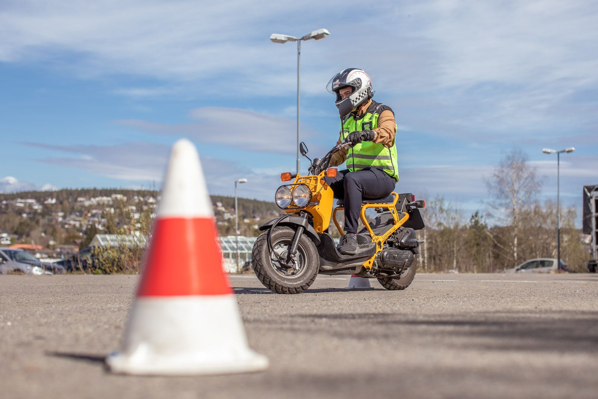 Motorsyklist som kjører en gul sykkel forbi en oransje og hvit kjegle på en åpen parkeringsplass
