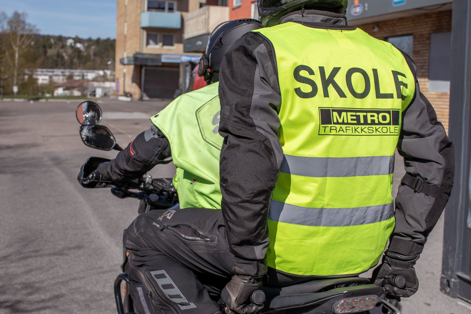 To Skole Metro-passasjerer i neongule sikkerhetsvester på motorsykkel ved en bygård