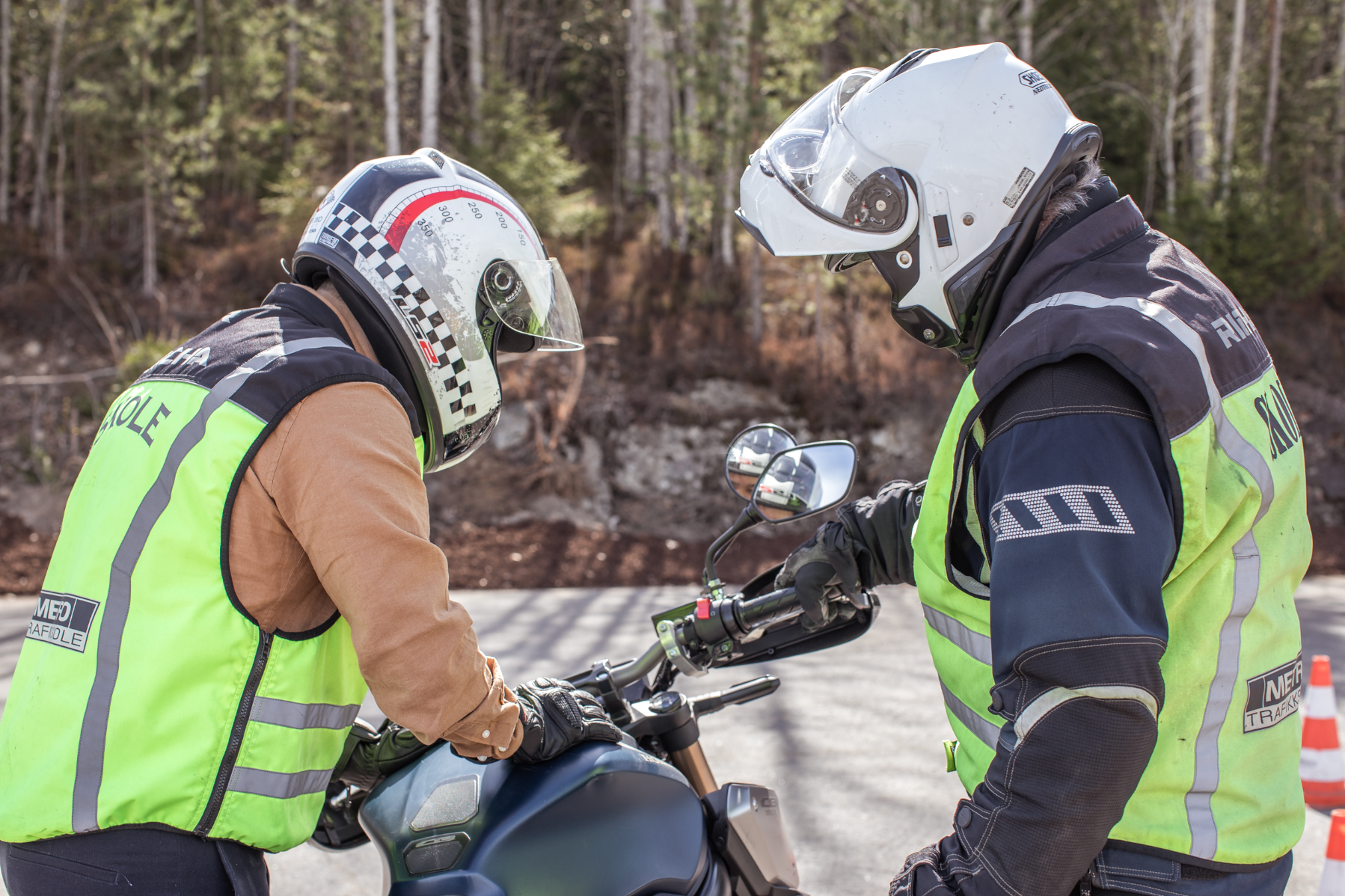 To hjelmkledde førere i refleksvester inspiserer en motorsykkel langs veien