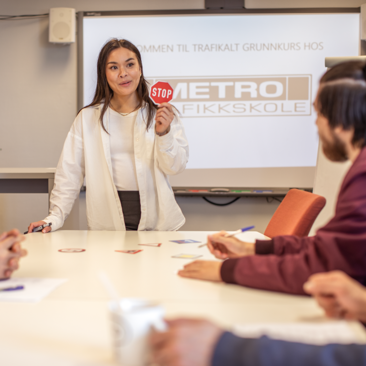 Kvinne som presenterer i et klasseromsmøte og peker på et stoppskiltgrafikk på en projeksjonsskjerm.