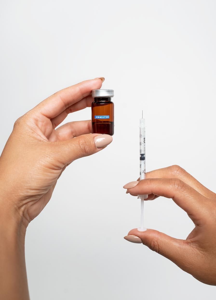 Syringe and small vial on a white tray, lit by soft natural light with blurred plants in the background