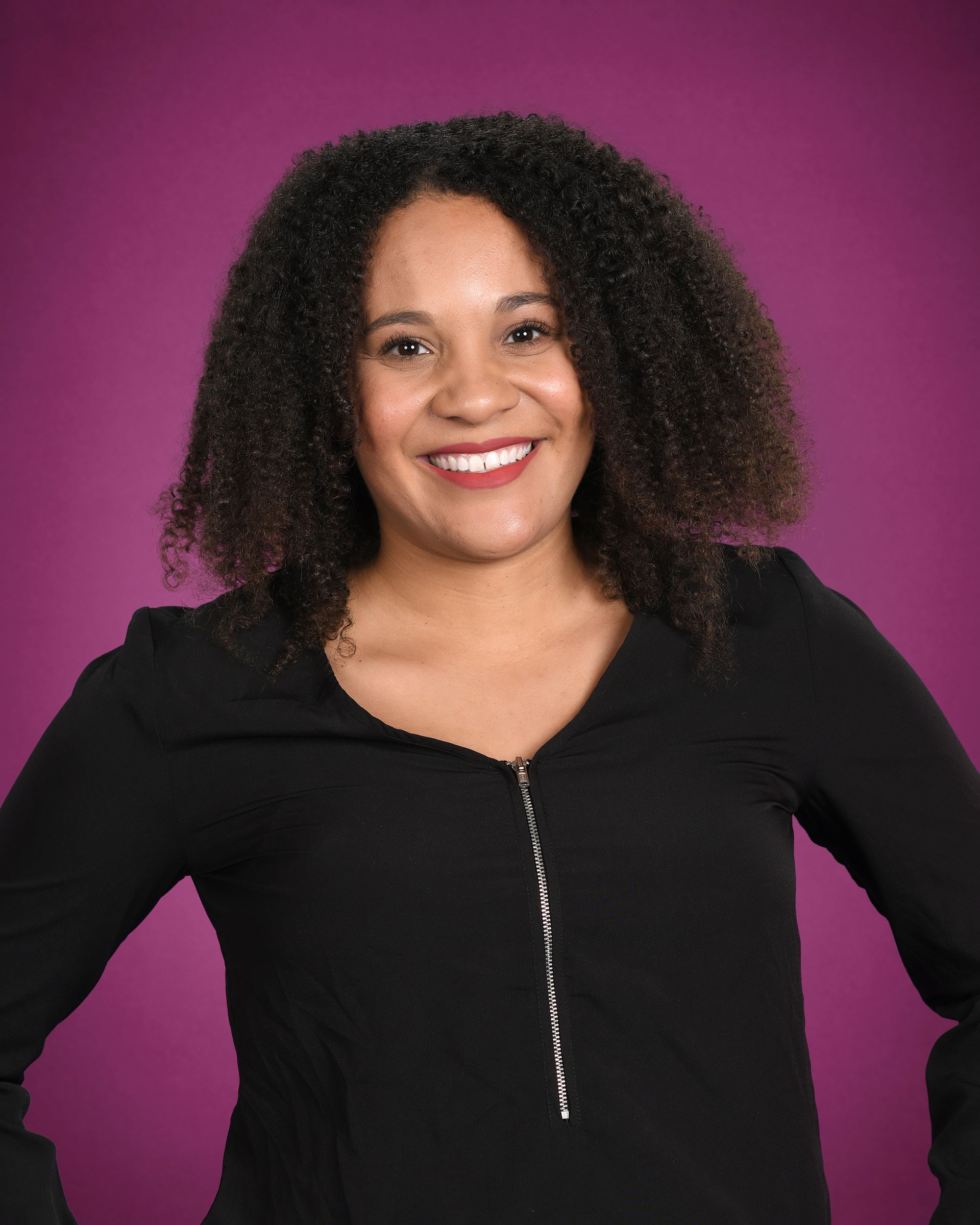 A woman with curly hair is wearing a black shirt and smiling.
