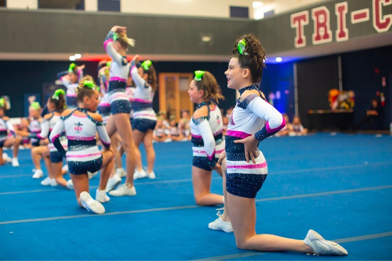 A group of cheerleaders are kneeling on the floor in a gym.