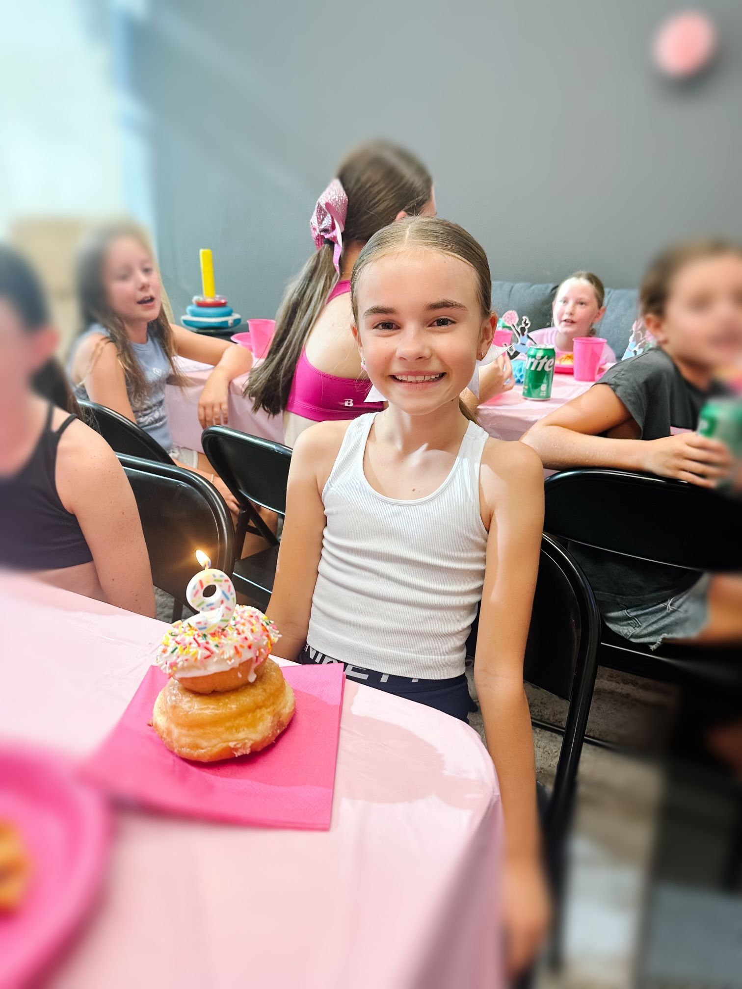 A young girl is sitting at a table with a donut and a candle on it.