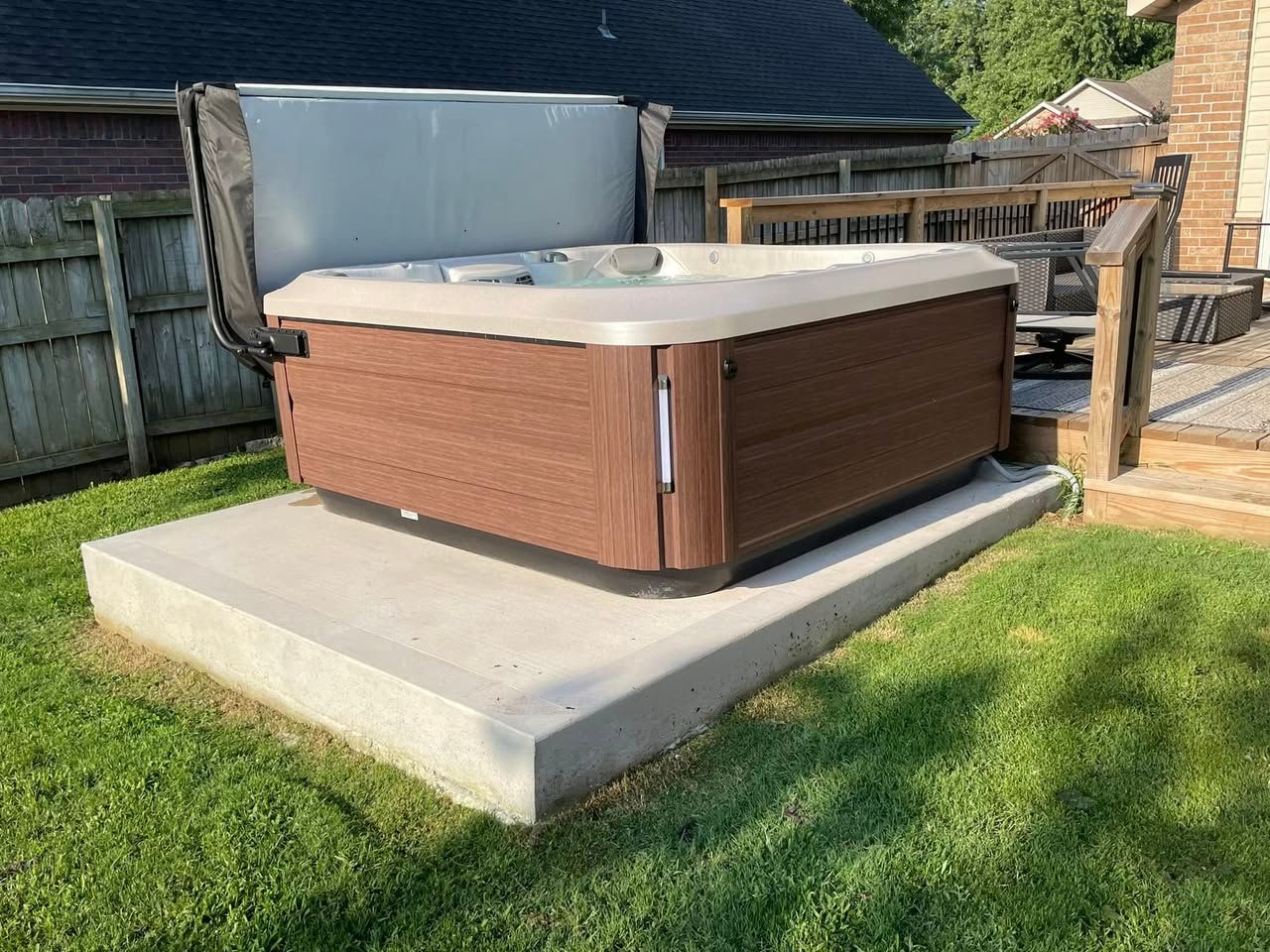 Outdoor hot tub on a concrete pad in a fenced backyard, with a white cover and brown siding.