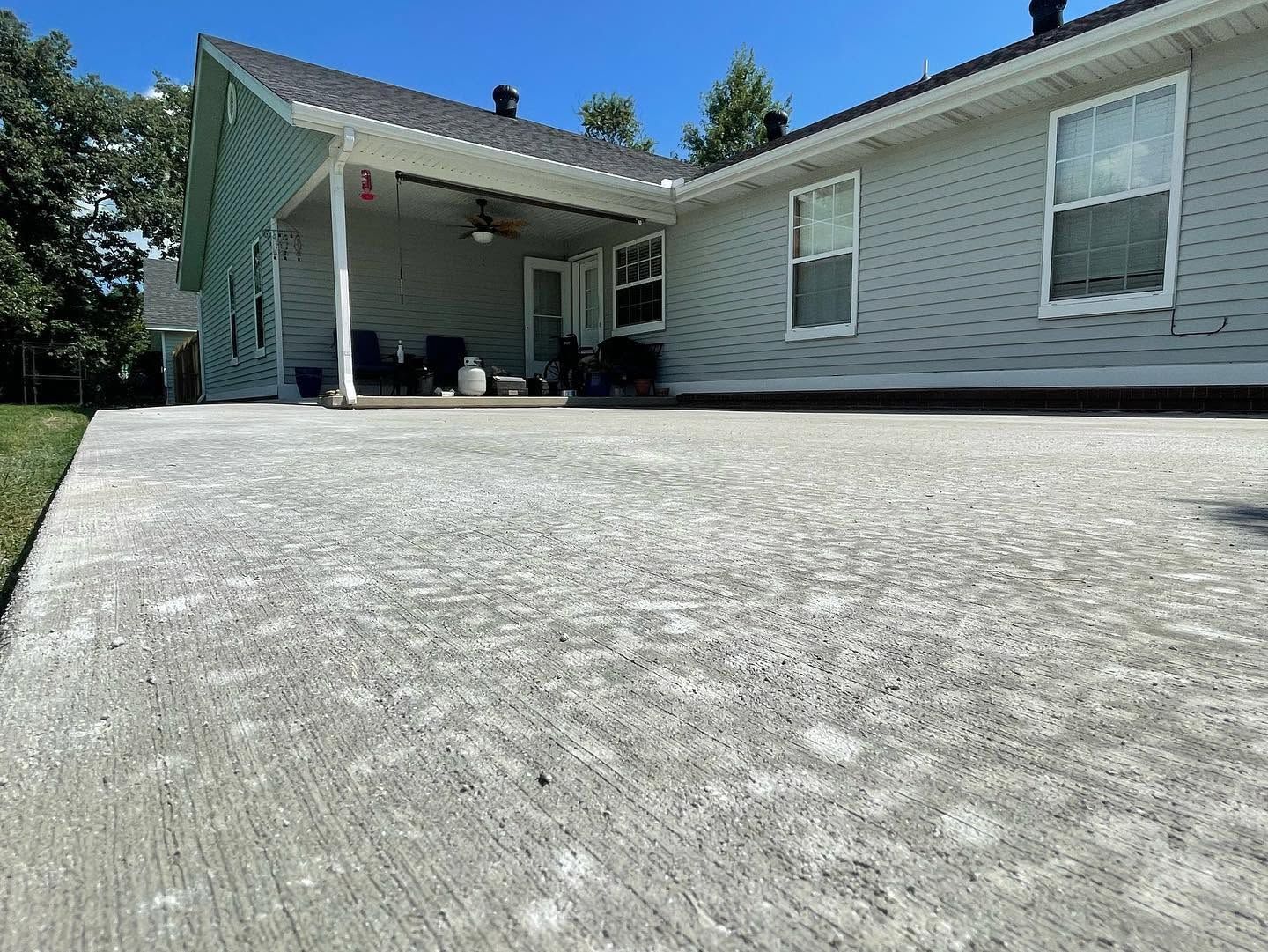 Wide concrete driveway leading to a white house with a covered porch on a sunny day