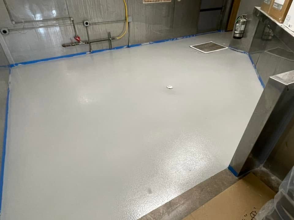 Empty industrial room with a smooth white floor coating and stainless steel fixtures