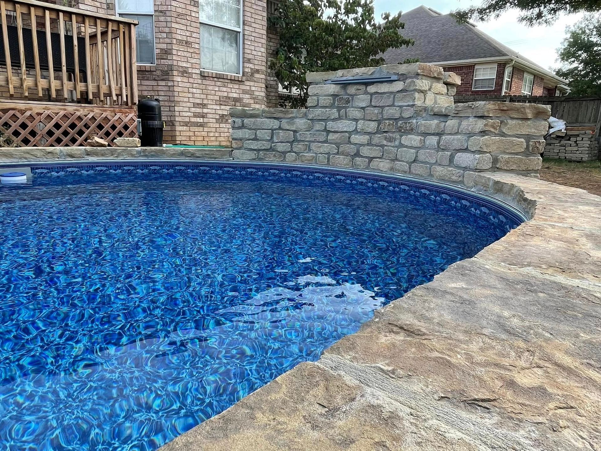Curved blue-tiled backyard pool beside a stone patio and house wall