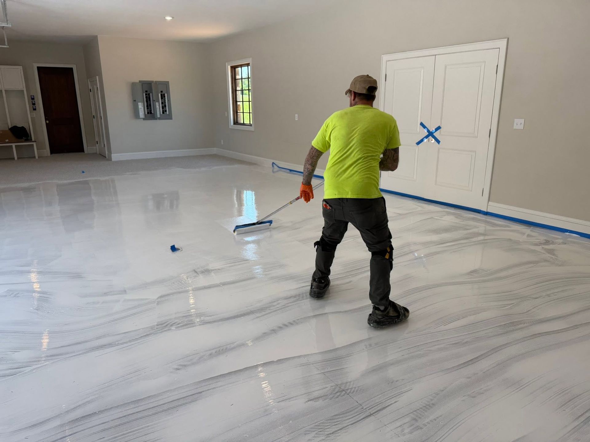 Worker in neon yellow shirt spreading coating on a floor in a large room under renovation