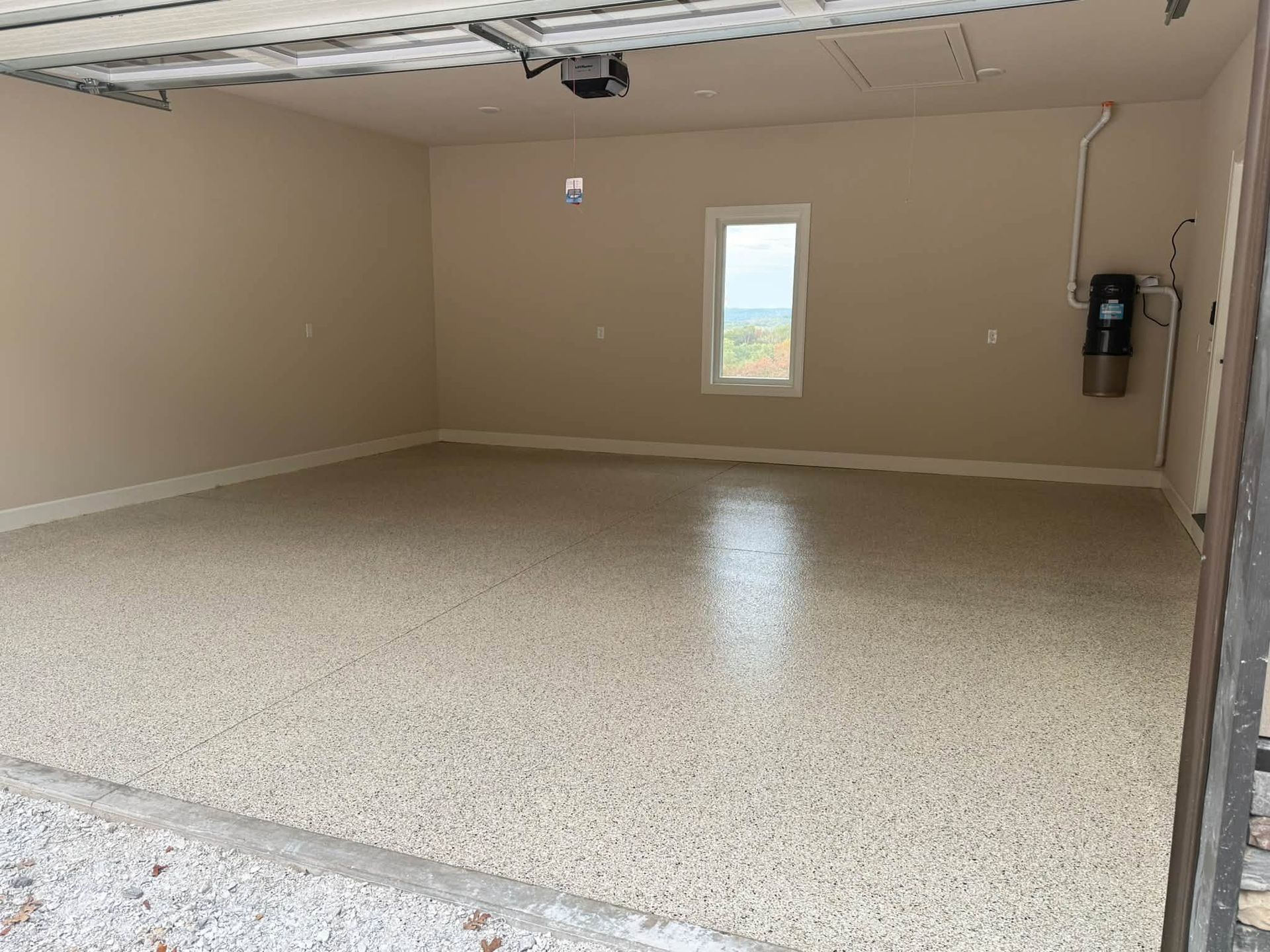 Empty beige garage with speckled epoxy floor, overhead door track, and a small window on the back wall