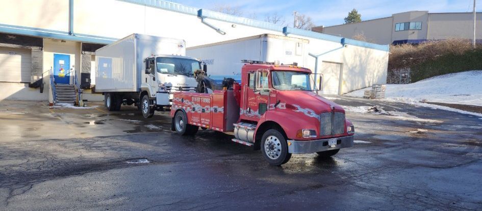 A red tow truck is parked next to a white truck in a parking lot.