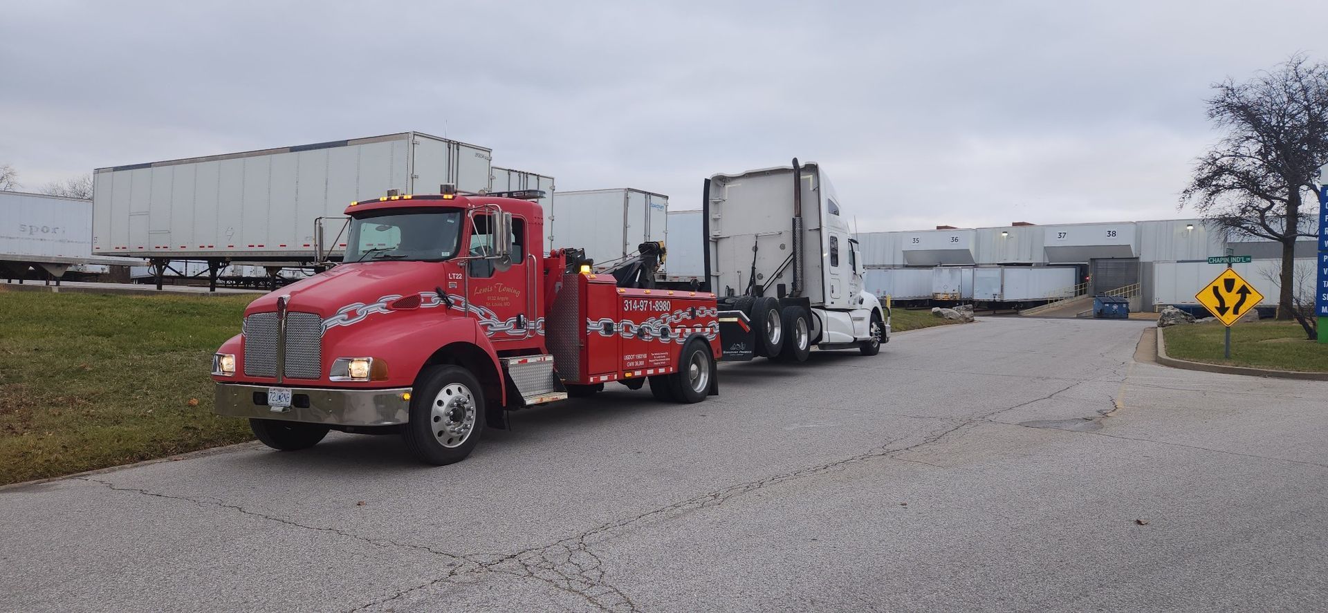 A red tow truck is towing a white semi truck down a road.