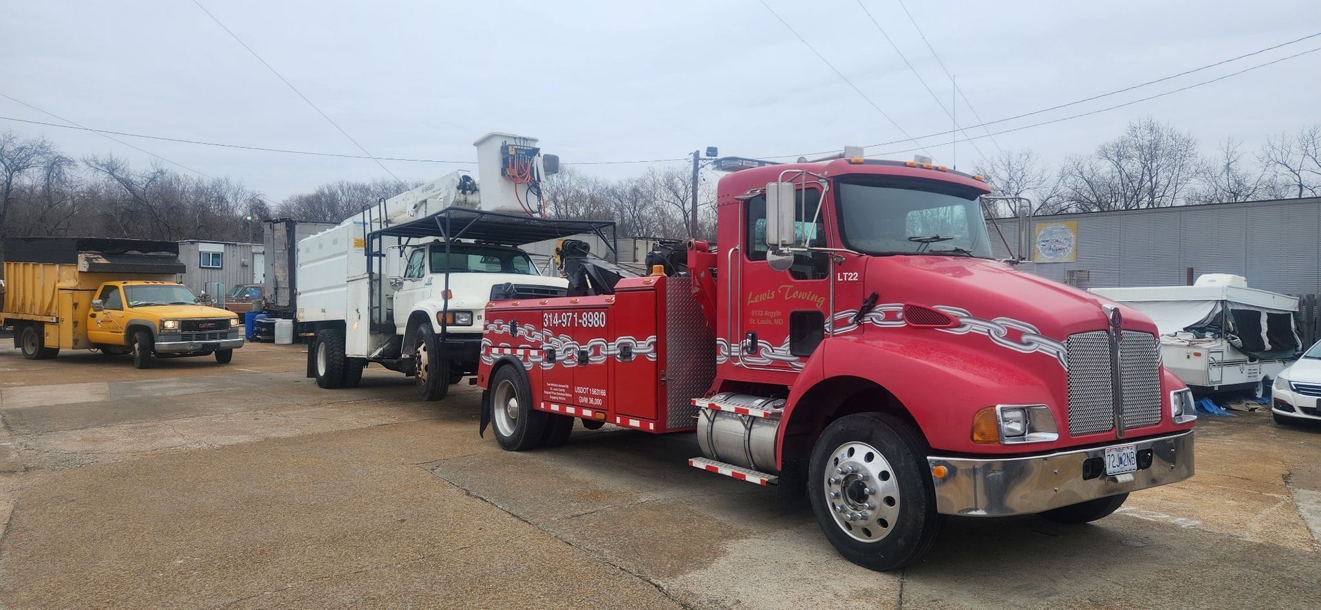 A red tow truck is parked next to a yellow dump truck.