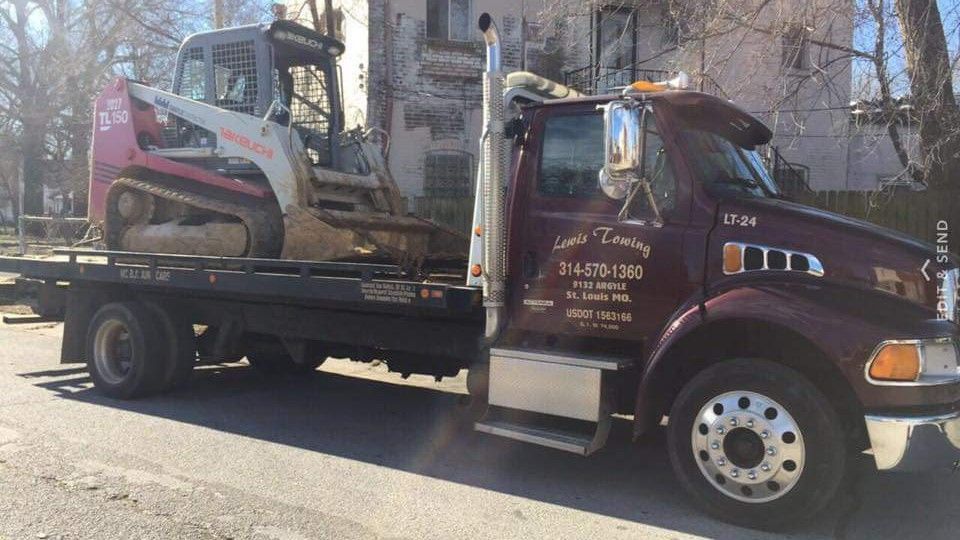 A tow truck with a bulldozer on the back is parked on the side of the road.