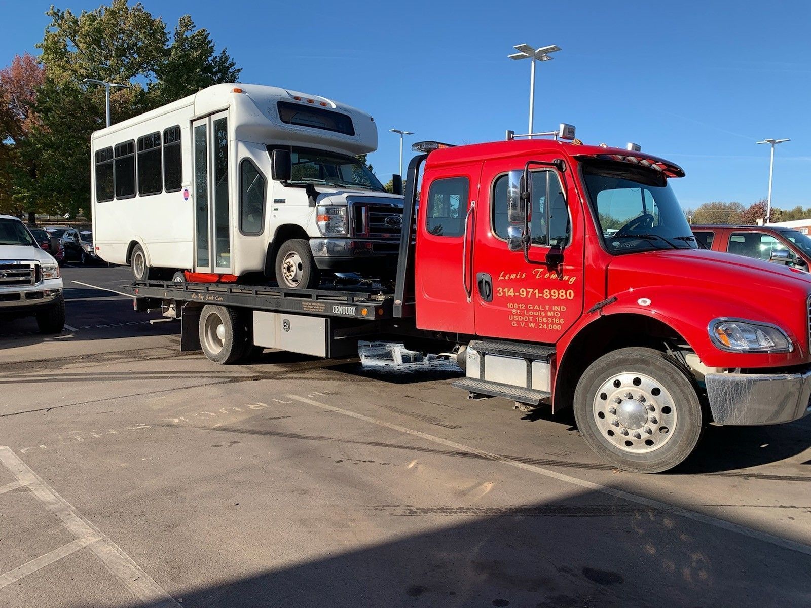 A red tow truck is towing a white bus in a parking lot.