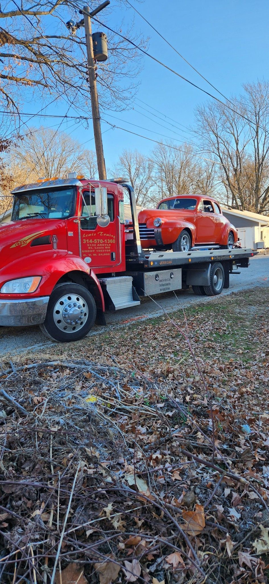 A red tow truck is towing a car on the back of it.