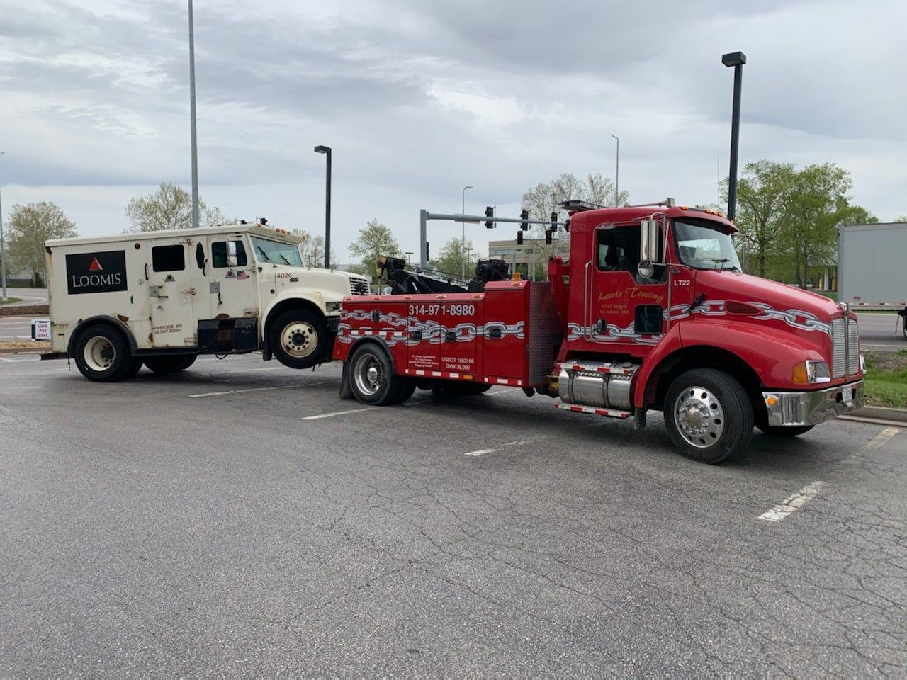 A red tow truck is towing a white armored vehicle.