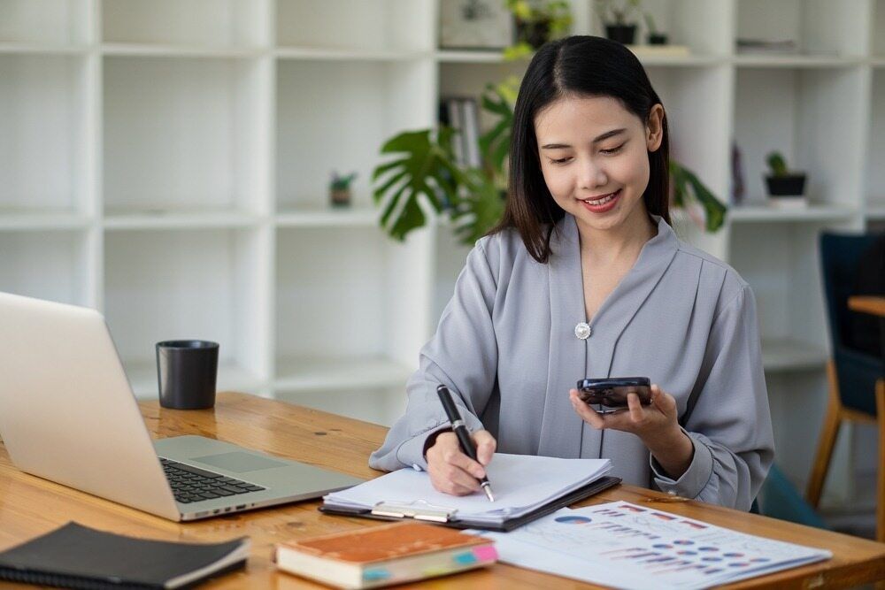 A Woman Is Sitting At A Desk With A Laptop And A Cell Phone — Visionary Accounting In Mudgee, NSW