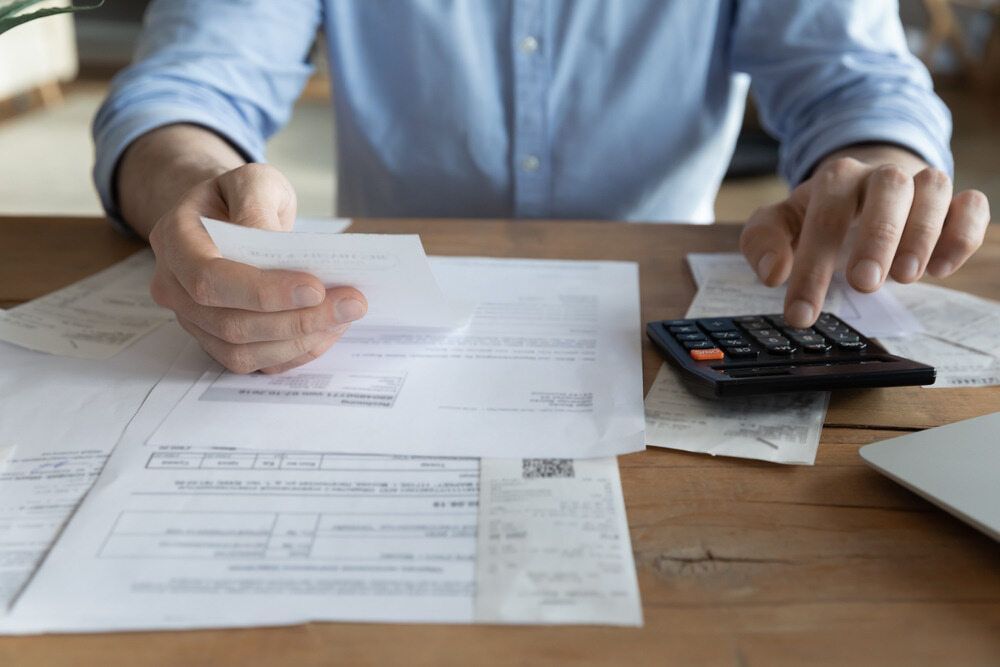 A Man Is Sitting At A Table Holding A Piece Of Paper And Using A Calculator — Visionary Accounting In Coonamble, NSW