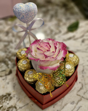Pequeña caja de regalo con flores rosas y blancas, un osito de peluche y bombones envueltos sobre una mesa.