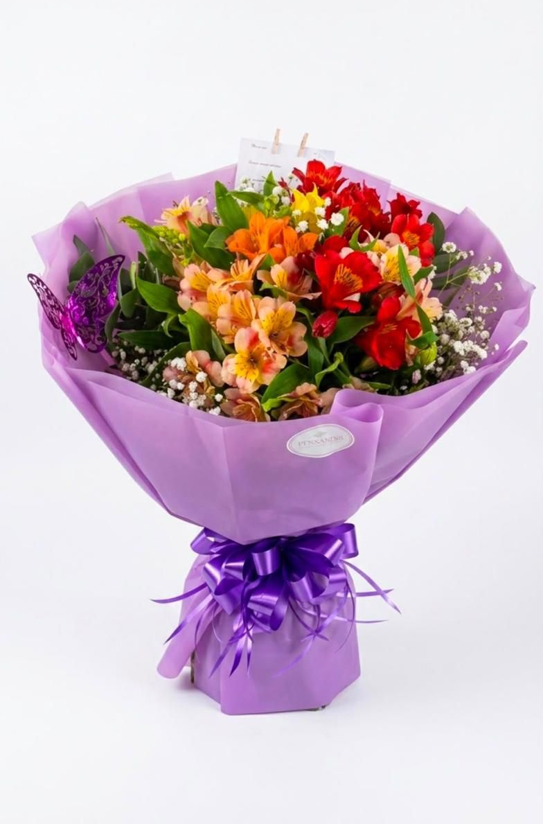 Ramo de flores variadas y coloridas envuelto en papel morado con una cinta a juego.