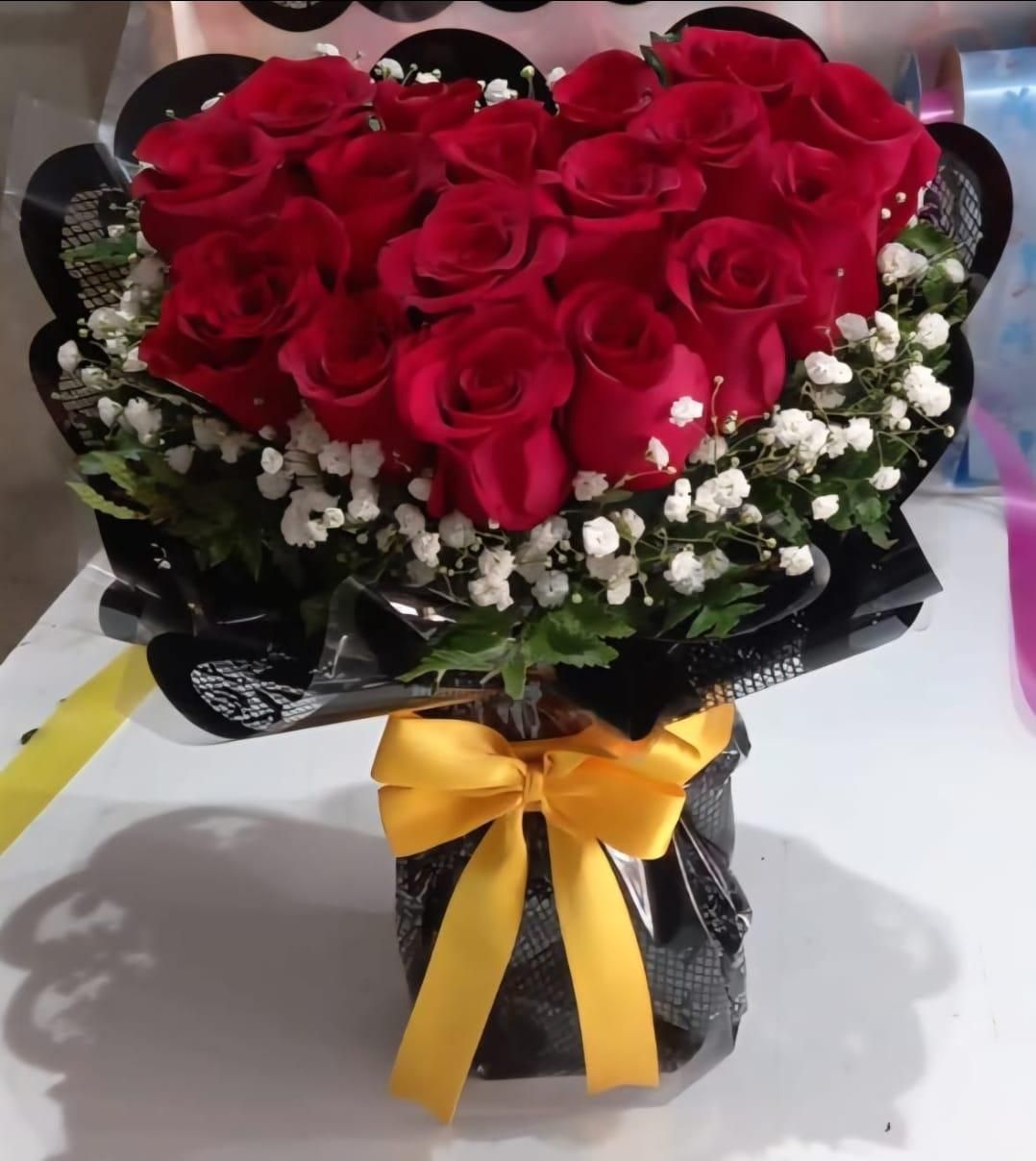 Ramo en forma de corazón de rosas rojas con paniculata en un jarrón negro, atado con una cinta dorada.