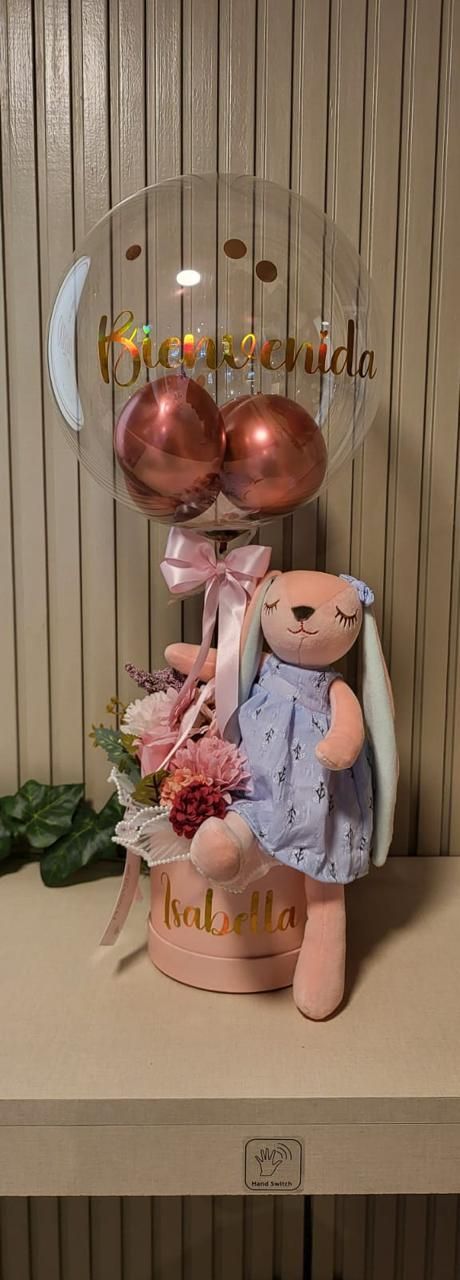 Arreglo floral de cumpleaños con osito de peluche rosa, globos y flores en una caja de regalo decorativa.