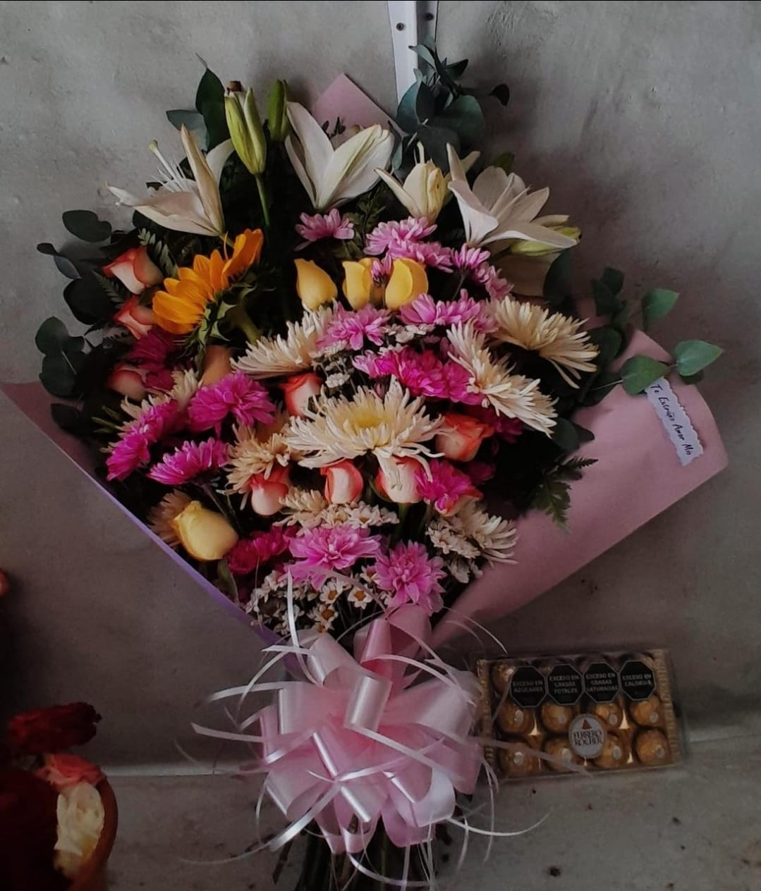 Ramo de flores variadas de colores, envuelto en papel rosa y adornado con una cinta